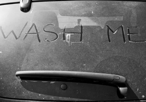 Messy car’s back window with “WASH ME” written into the dirty surface